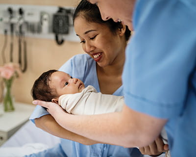 Newborn baby, mother and clinician in hospital room