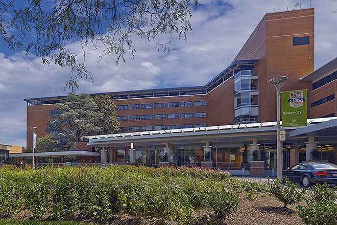Outside view of Lankenau Medical Center building front with tall, green grass in the foreground and a blue sky behind it. 